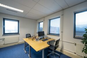 Modern ingericht kantoor aan de Joop Geesinkweg met twee bureaus, een computer en uitzicht op kantoorgebouwen.